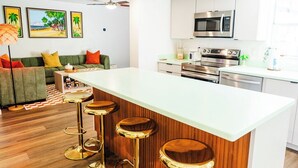 A modern kitchen with a central island, bar stools, and a ceiling fan. - The Tiki Palm- Screened Pool, Mini Golf, Arcade & Creekside Fun (Longwood)