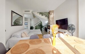 A modern living room with a sofa, a dining table with placemats, a TV, and a staircase leading to an upper level. - Luxurious home in Alhaurín de la Torre (Alhaurín de la Torre)