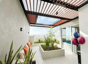 En moderne balkon med udendørs møbler, træpergola, plantekasse med planter og hyggekroge med puder.