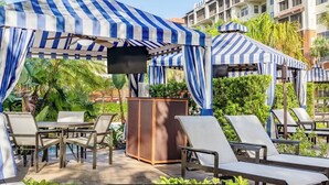 Ein Poolbereich mit Streifenmarkisen, Liegestühlen und einem Holzkasten.