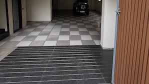 A spacious indoor area with a checkered floor, a parked vehicle, and a closed wooden door. - Nele comforts (Bengaluru,)