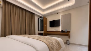 A modern hotel room with a large bed, a flat-screen TV, a wooden dresser, and a mirror. - Nele comforts (Bengaluru,)