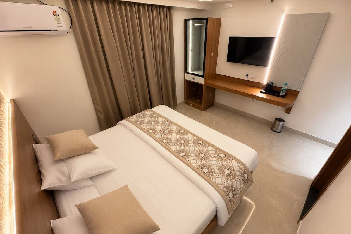 Quarto de hotel com cama, televisão, espelho e um banco de madeira.