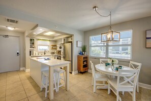 A modern kitchen with white cabinetry, a central island, and a dining area with white chairs. - Beach Villas 101 Beachfront Condo: Heated Pool, Walk to Dwtn (Fort Myers Beach)