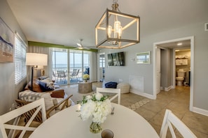 A living room with a dining table, chairs, a sofa, a lamp, a chandelier, and a view of the outdoors. - Beach Villas 101 Beachfront Condo: Heated Pool, Walk to Dwtn (Fort Myers Beach)