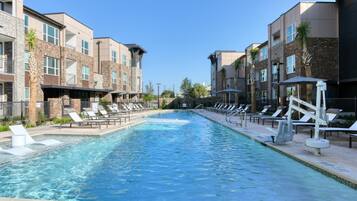 A swimming pool with lounge chairs and a brick building with multiple windows.