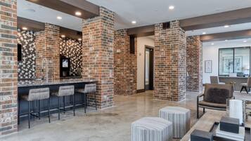 A modern kitchen with a brick accent wall, a bar area with stools, and a seating area with ottomans.