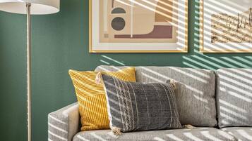 A living room with a sofa, two pillows, a floor lamp, and framed artwork on the wall.