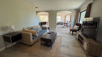 Een woonkamer met een bank, salontafel, televisie en een eethoek op de achtergrond.