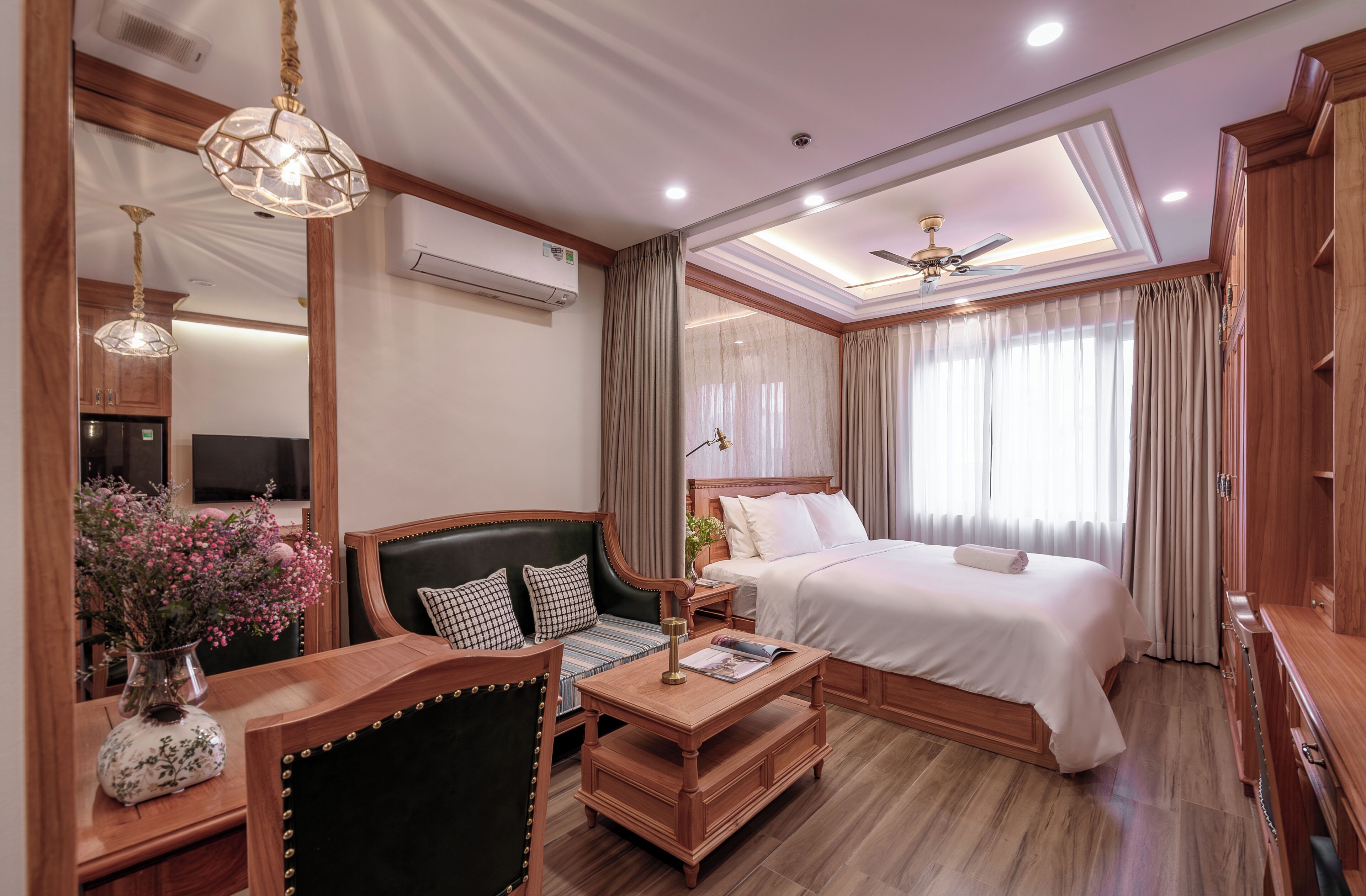 Une chambre d’hôtel équipée d’un lit, d’un bureau, d’une chaise, d’une télévision, d’un ventilateur de plafond et d’une fenêtre avec des rideaux.