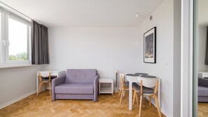Una sala de estar moderna con un sofá, una mesa de comedor, sillas, una mesita blanca y un cuadro en la pared.