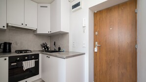 Una cocina con armarios blancos, horno empotrado, cafetera y puerta de madera.