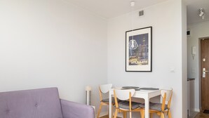 Una sala de estar moderna con un sofá púrpura, una mesa de comedor con sillas, un cuadro enmarcado con una vista urbana y suelo de madera.