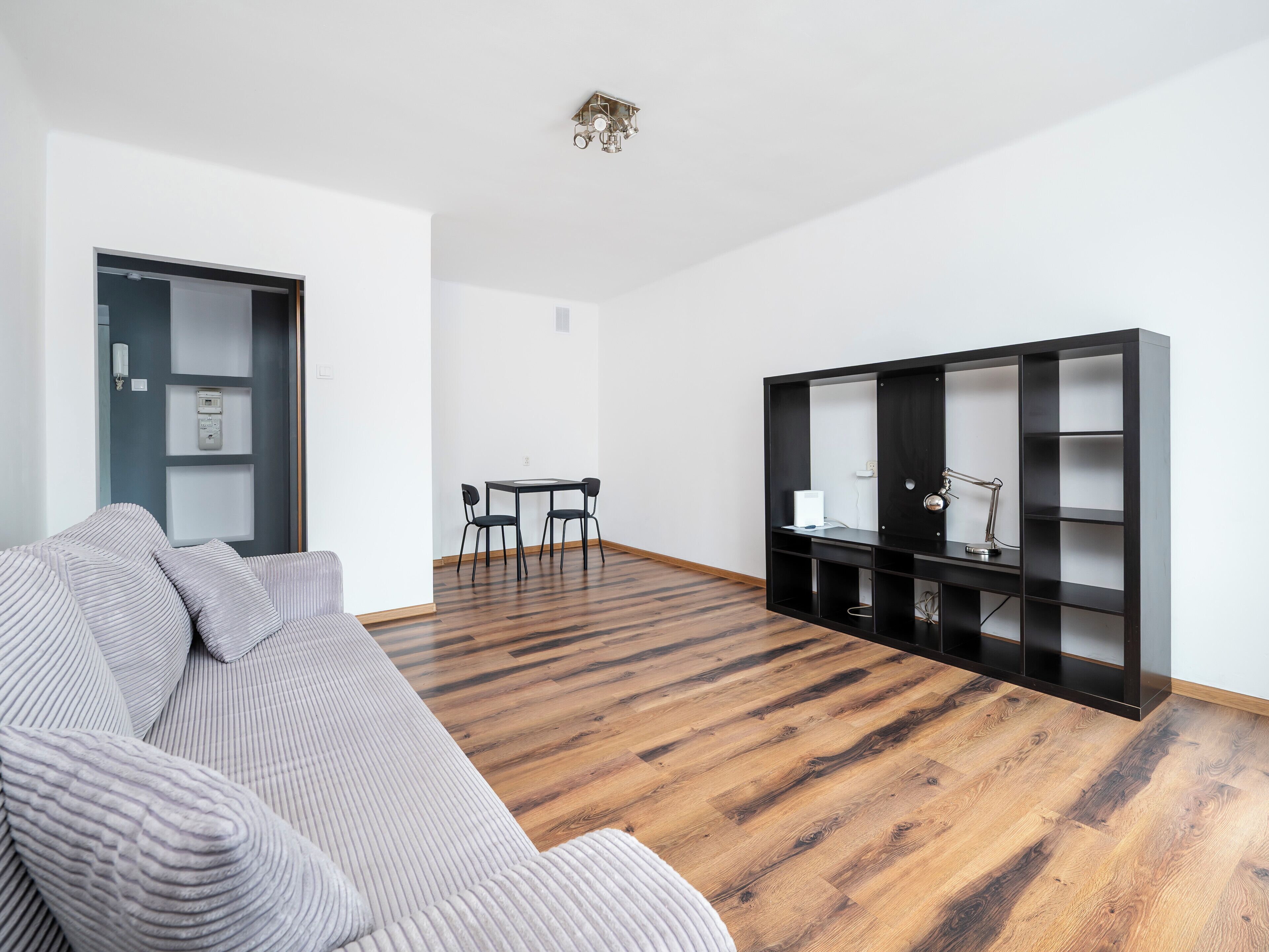 Una sala de estar moderna con un sofá, una mesa de comedor con sillas, una estantería negra y suelo de madera.