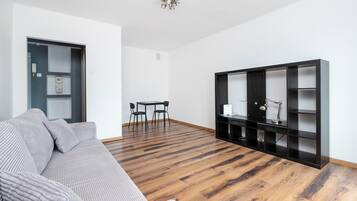 Una sala de estar moderna con un sofá, una mesa de comedor con sillas, una estantería negra y suelo de madera.