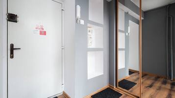 Habitación de hotel con una puerta blanca, un felpudo negro, suelo de madera y un espejo grande.