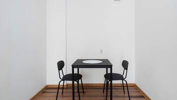 A room with a dark wooden floor, a white wall, and a black table with two chairs.