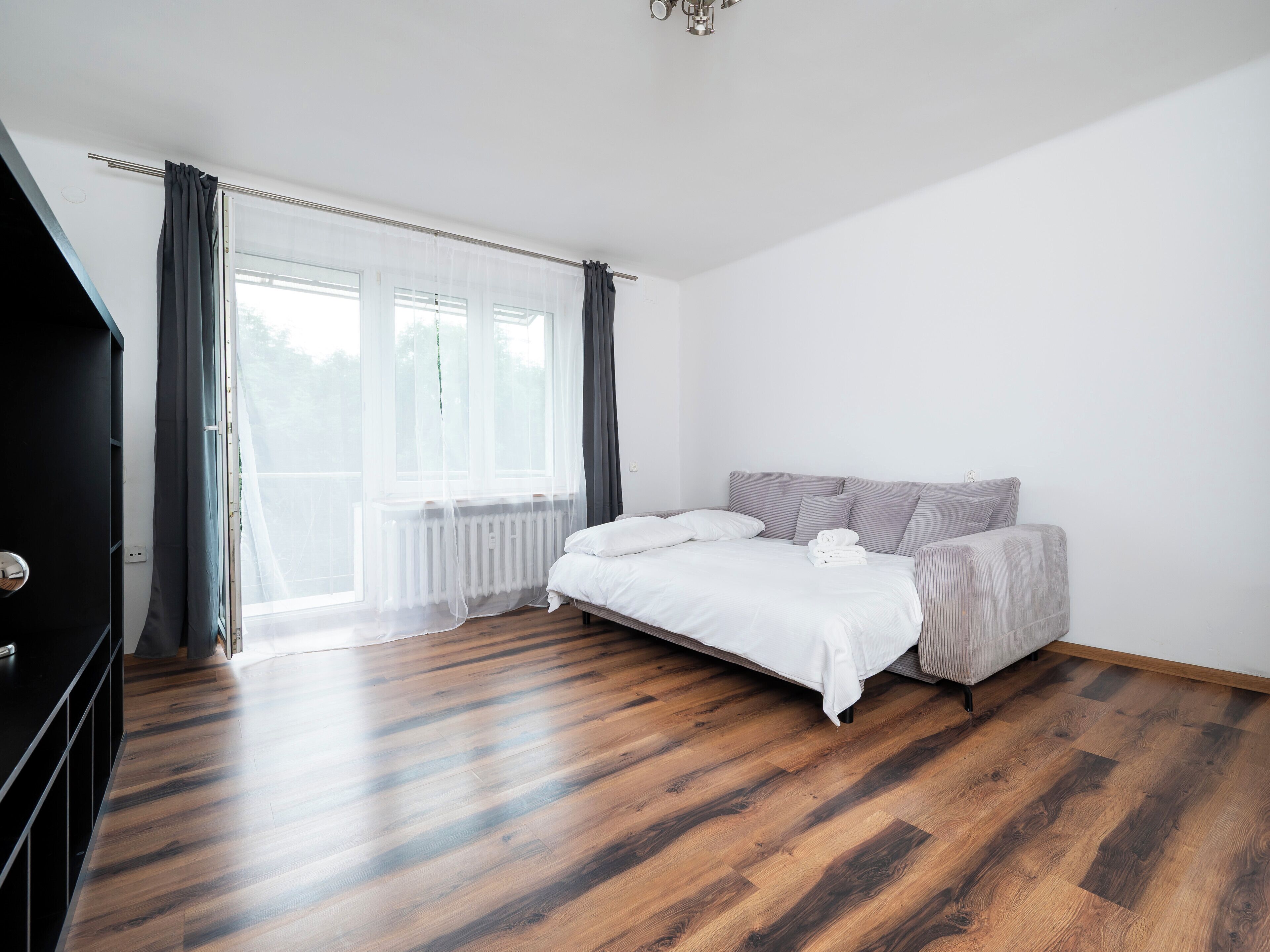 Un dormitorio con cama, sofá, radiador y ventana con cortinas.