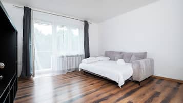 Un dormitorio con cama, sofá, radiador y ventana con cortinas.