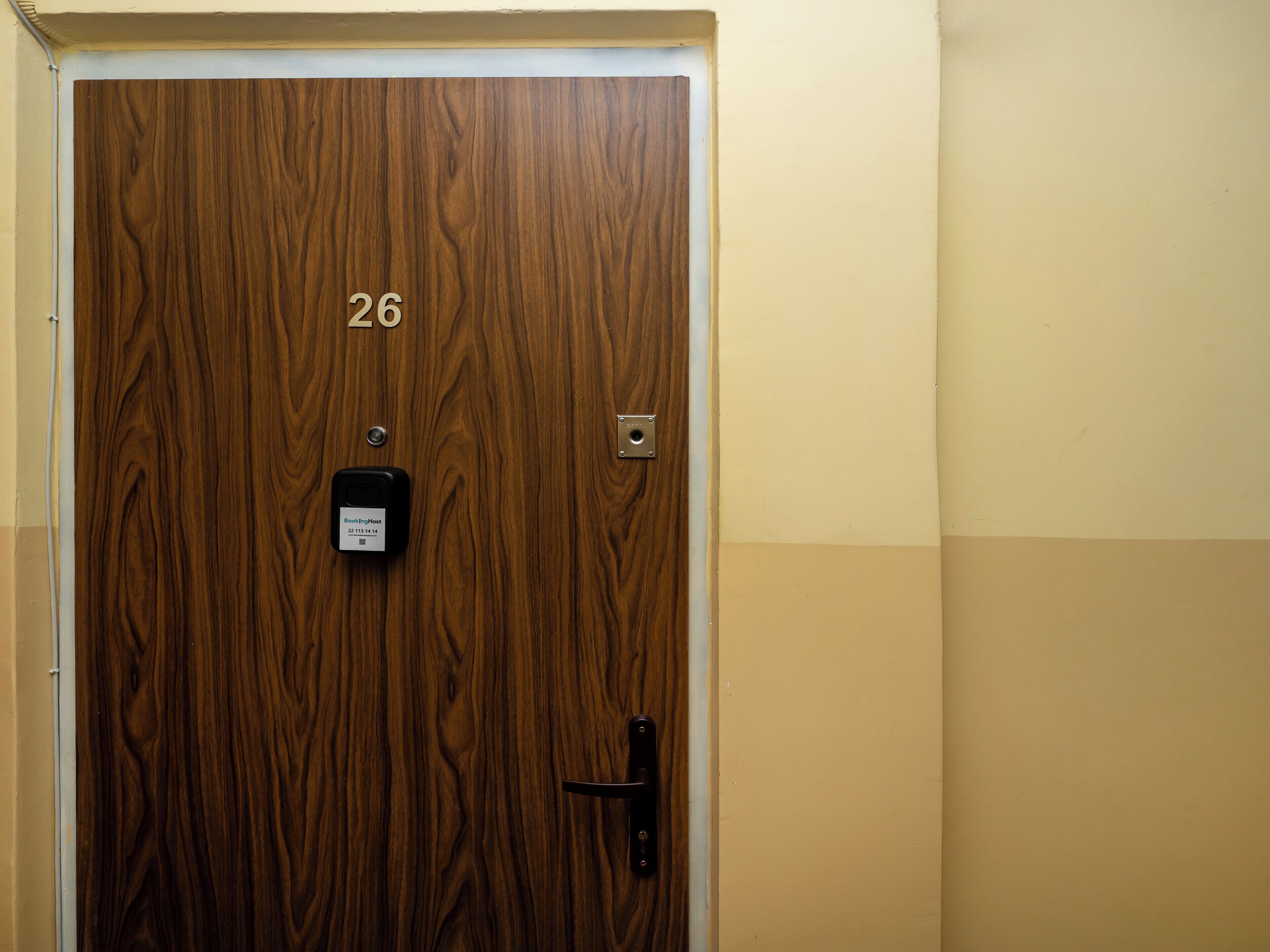 Une porte en bois portant le numéro 26, un interphone et un trou de serrure.