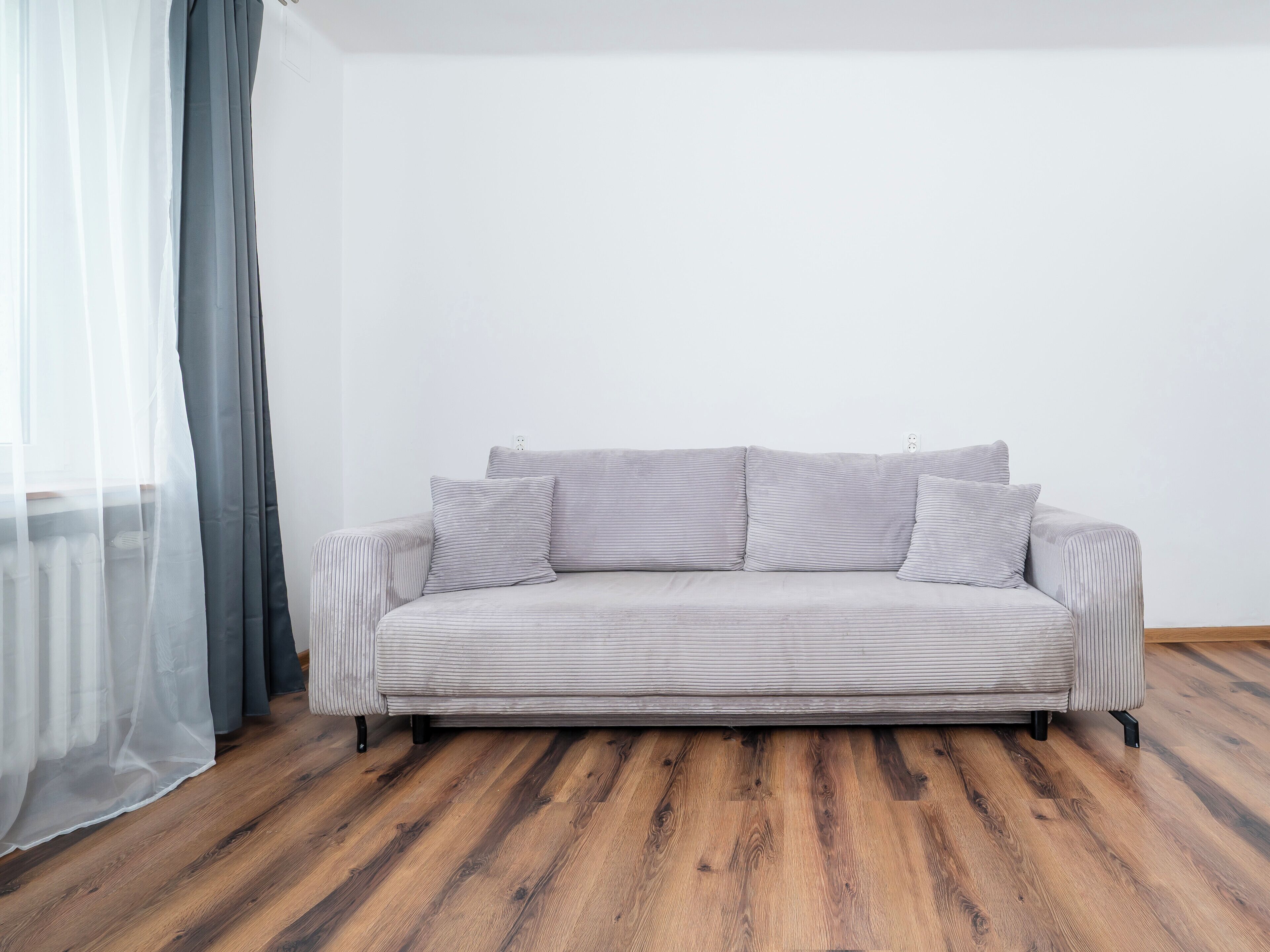 A sofa with striped cushions in a room with wooden flooring and a white wall.