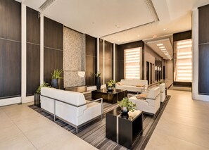 Eine moderne Hotelhalle mit Sitzgelegenheiten, einem Empfangstresen und einer großen Wand mit strukturierter Oberfläche.