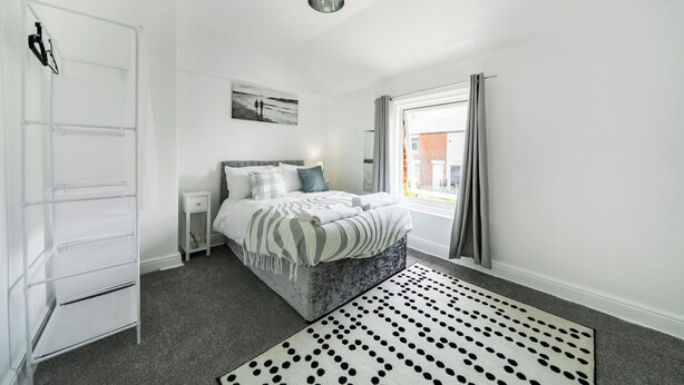 Een slaapkamer met een bed, een witte garderobe, een nachtkastje, een kamerbreed tapijt met patroon en een raam met gordijnen.
