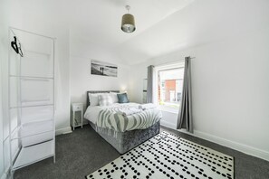 Une chambre à coucher avec un lit, une armoire blanche, une table de chevet, un tapis à motifs et une fenêtre avec des rideaux.