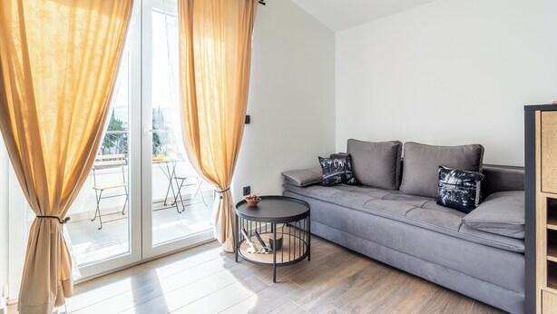 Ein modernes Wohnzimmer mit einem grauen Sofa, einem kleinen runden Tisch und einer Schiebetür mit Vorhängen.