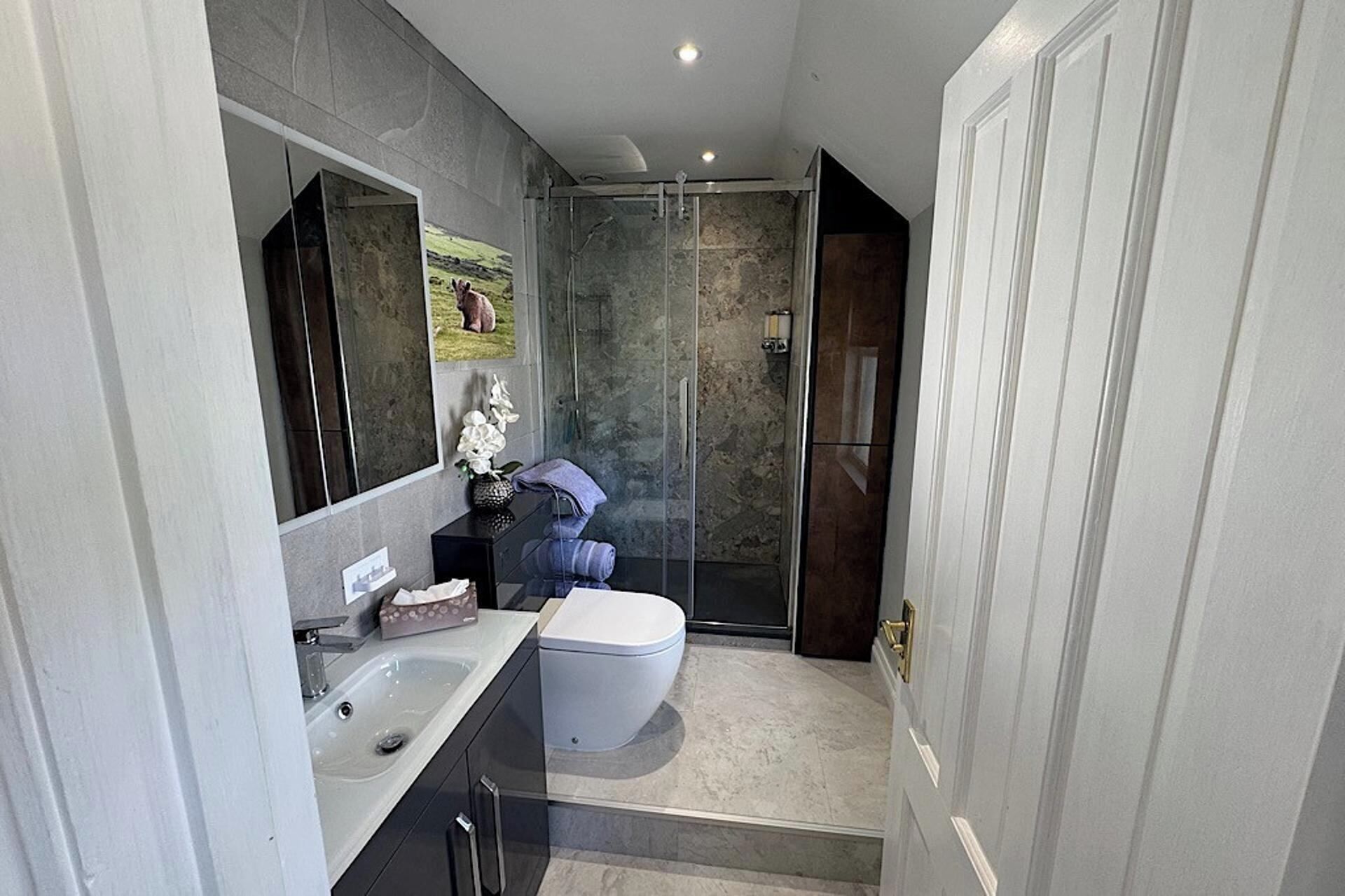 A modern bathroom with a glass shower enclosure, a white toilet, and a sink with a marble countertop.