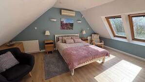 Quarto com teto inclinado, uma cama, uma cadeira, um radiador e uma janela.