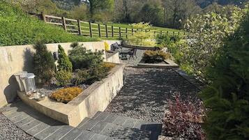 A landscaped garden with a stone pathway, seating area, and a wooden fence.