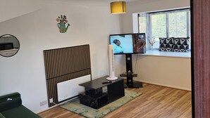 A modern living room with a green sofa, a TV, a standing fan, and a window with a view of trees.