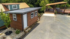 A small wooden cabin with a metal roof, a covered outdoor seating area, and a paved driveway. - 30-Unit Tiny Home Village | Sleeps 100+ | Sojourn Lodging (Sevierville)