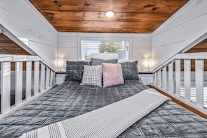 A bedroom with a bed, pillows, a bedside lamp, and a window. - 30-Unit Tiny Home Village | Sleeps 100+ | Sojourn Lodging (Sevierville)
