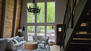 Un salon spacieux avec une grande fenêtre, un escalier et un lustre moderne.