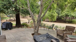 Une terrasse en bois avec des meubles en osier, un barbecue couvert et un arbre.