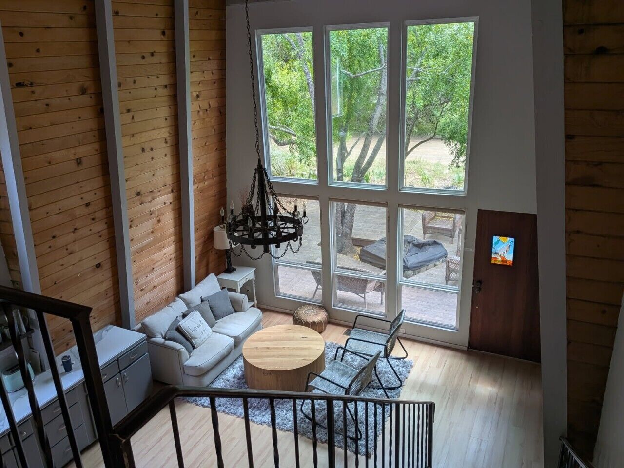 A spacious living area with a large window, a sofa set, a round coffee table, and a hanging light fixture.