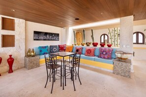Ein Essbereich mit Tisch und Stühlen, einer Steinwand und einem farbenfrohen Sofa mit Kissen.