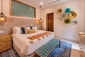 A bedroom with a bed, bedside tables, a bench, a patterned rug, decorative wall plates, and a patterned wall. - Breathtaking Cabo Villa | Epic Golf & Ocean Views (Cabo San Lucas)