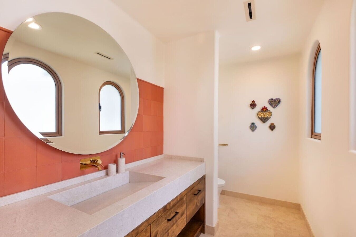 A bathroom with a large round mirror, a white sink, a wooden vanity, and a toilet.