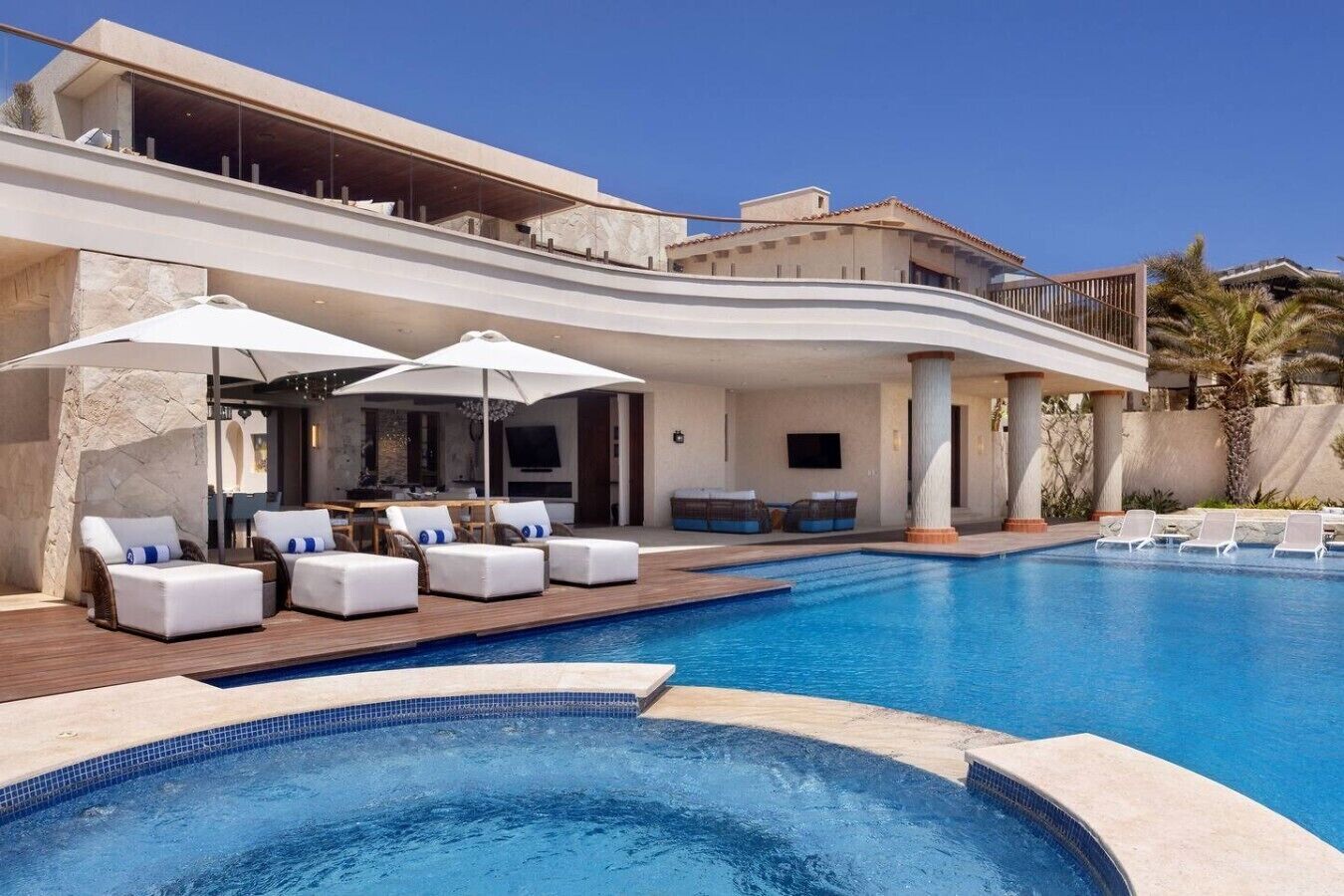 Un área de piscina moderna con sillones de descanso y sombrillas, una piscina y un edificio con techo curvo.