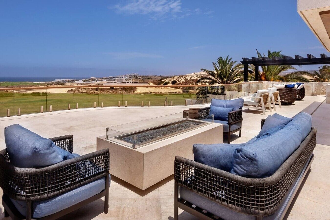 A patio with wicker furniture, a fire pit, and a view of the beach.