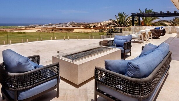 Eine Terrasse mit Korbmöbeln, einer Feuerstelle und Blick auf den Strand.