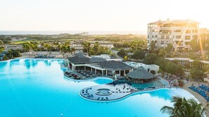 Ein Resort mit einem großen Schwimmbecken, mehreren Liegebereichen und einem Gebäude mit weißer Fassade.