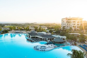 Ein Resort mit einem großen Schwimmbecken, mehreren Liegebereichen und einem Gebäude mit weißer Fassade.
