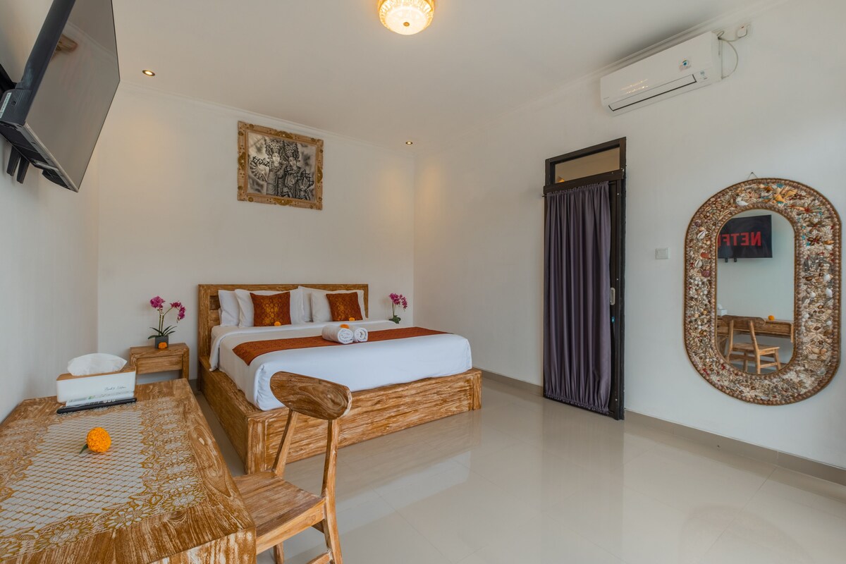 Habitación de hotel con cama, escritorio, silla, espejo y unidad de aire acondicionado.