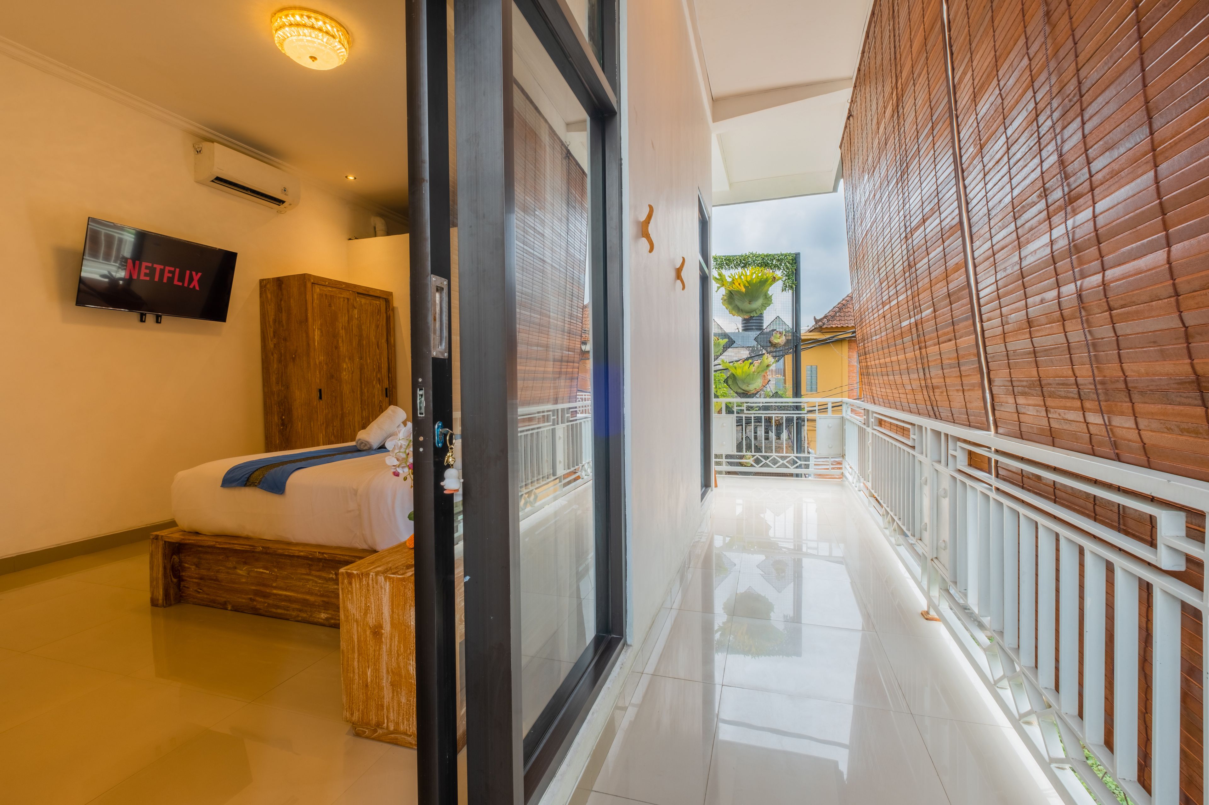 A hotel corridor with a bed, a television displaying 'NETFLIX', and a view of the outside balcony.