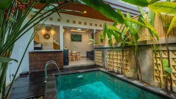 Une piscine dotée d’une terrasse en bois, entourée de plantes tropicales et agrémentée d’un espace salon abrité.
