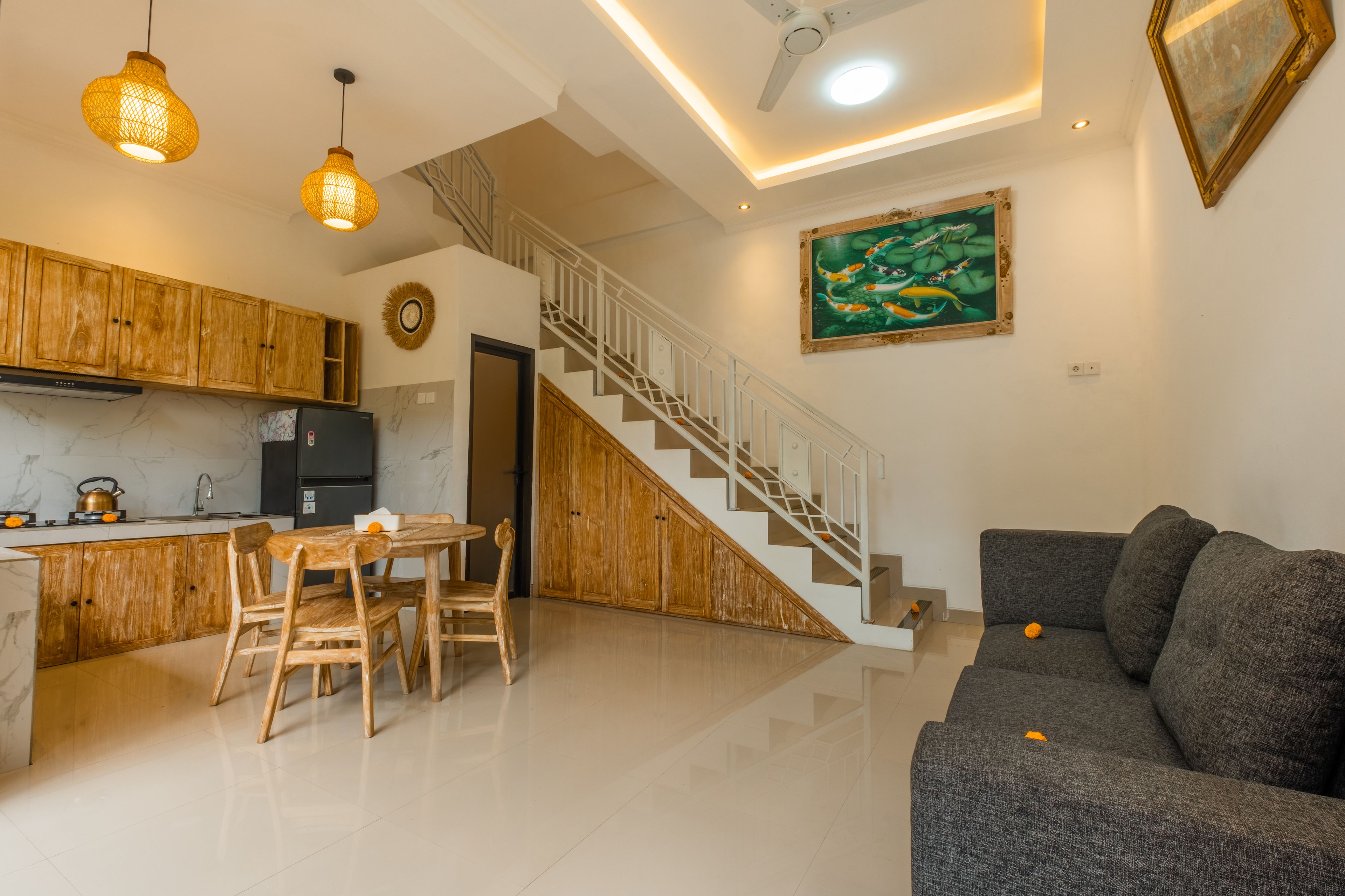 A modern kitchen with wooden cabinets, a dining area with a table and chairs, a staircase, and a living room with a sofa.